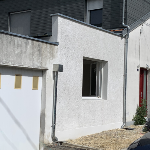 Façade d'une maison individuelle modernisée avec un mur blanc enduit et une extension de gros œuvre réalisée par l'entreprise Meyer.